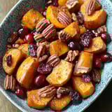A serving bowl of roasted butternut squash with cranberries and pecans, lightly glazed for sweetness.