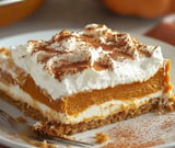 A rich pumpkin dessert slice topped with whipped cream and sprinkled with cinnamon on a cookie crust.