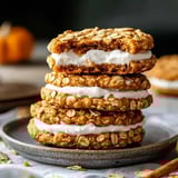 Several soft oatmeal cookies with white filling stacked on a gray plate, one with a bite missing.