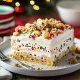 A layered treat slice with cookie crumbs, bright sprinkles, cherries, and whipped topping served on a plate with a fork.