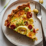 A slice of pie filled with leeks and chorizo on a plate, with a fork beside it.