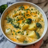 A bowl of creamy potato and broccoli soup topped with shredded cheddar and fresh chives.