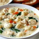 A bowl of creamy gnocchi soup with tender chicken pieces, carrots, and spinach.