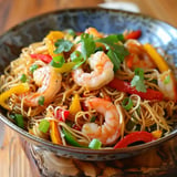 A colorful dish of noodles topped with shrimp and fresh vegetables served in a bowl.