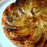 A spiral design of caramelized onion tart served on a plate.