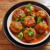 A dish of flavorful chicken balls in a red curry, garnished with fresh coriander and sesame seeds.